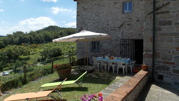 A stone building with a patio area featuring outdoor furniture, a table set for dining, and a view of a lush green landscape.