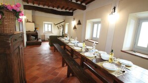 A long wooden dining table set for a meal, with a rustic kitchen in the background.