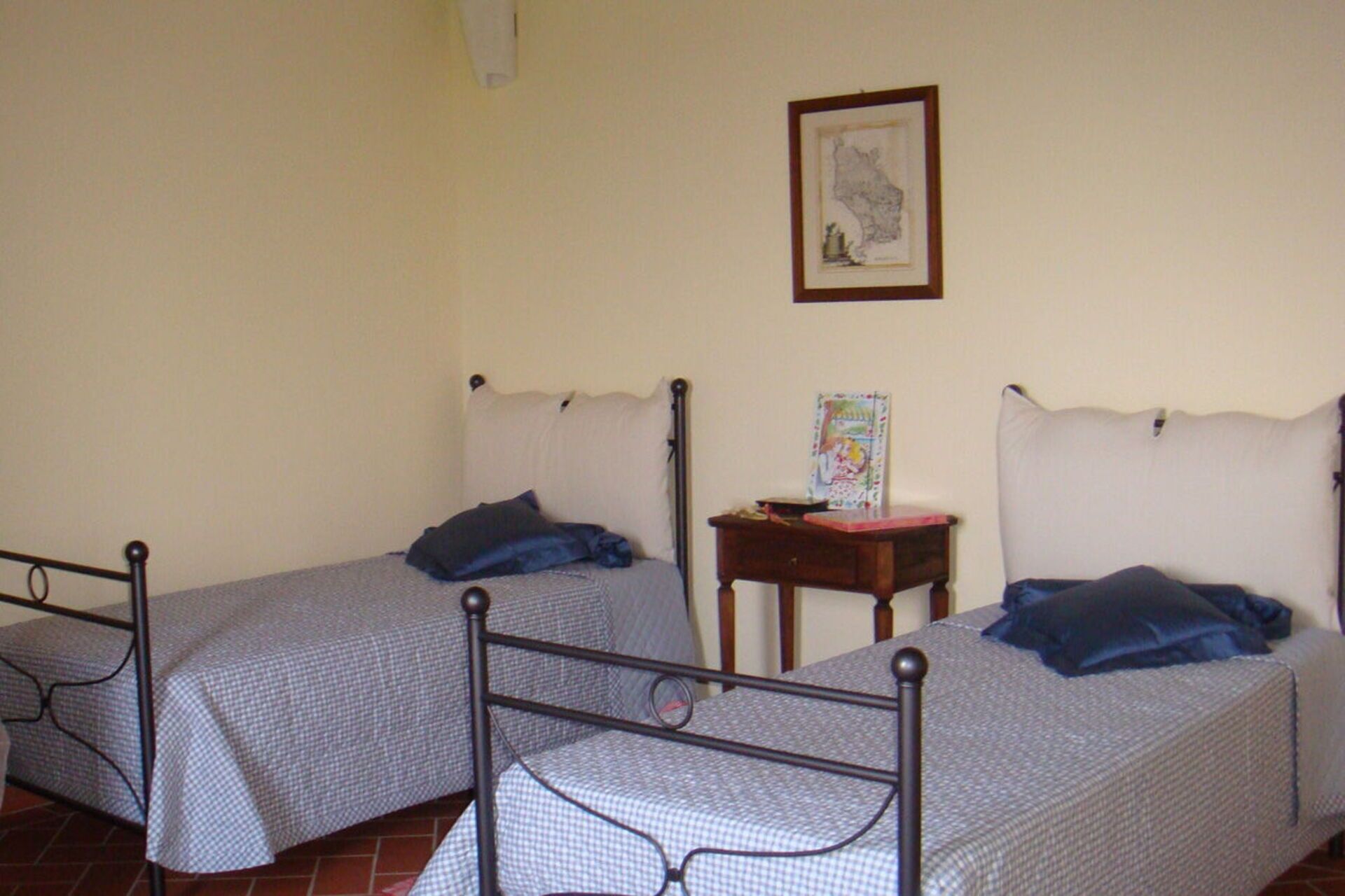 Two single beds with headboards, a small wooden table, and a framed picture on the wall.