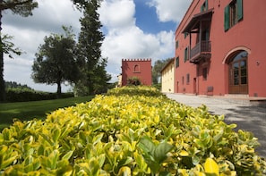 Ein rotes Gebäude mit einem Turm, umgeben von gepflegten Hecken und Bäumen.