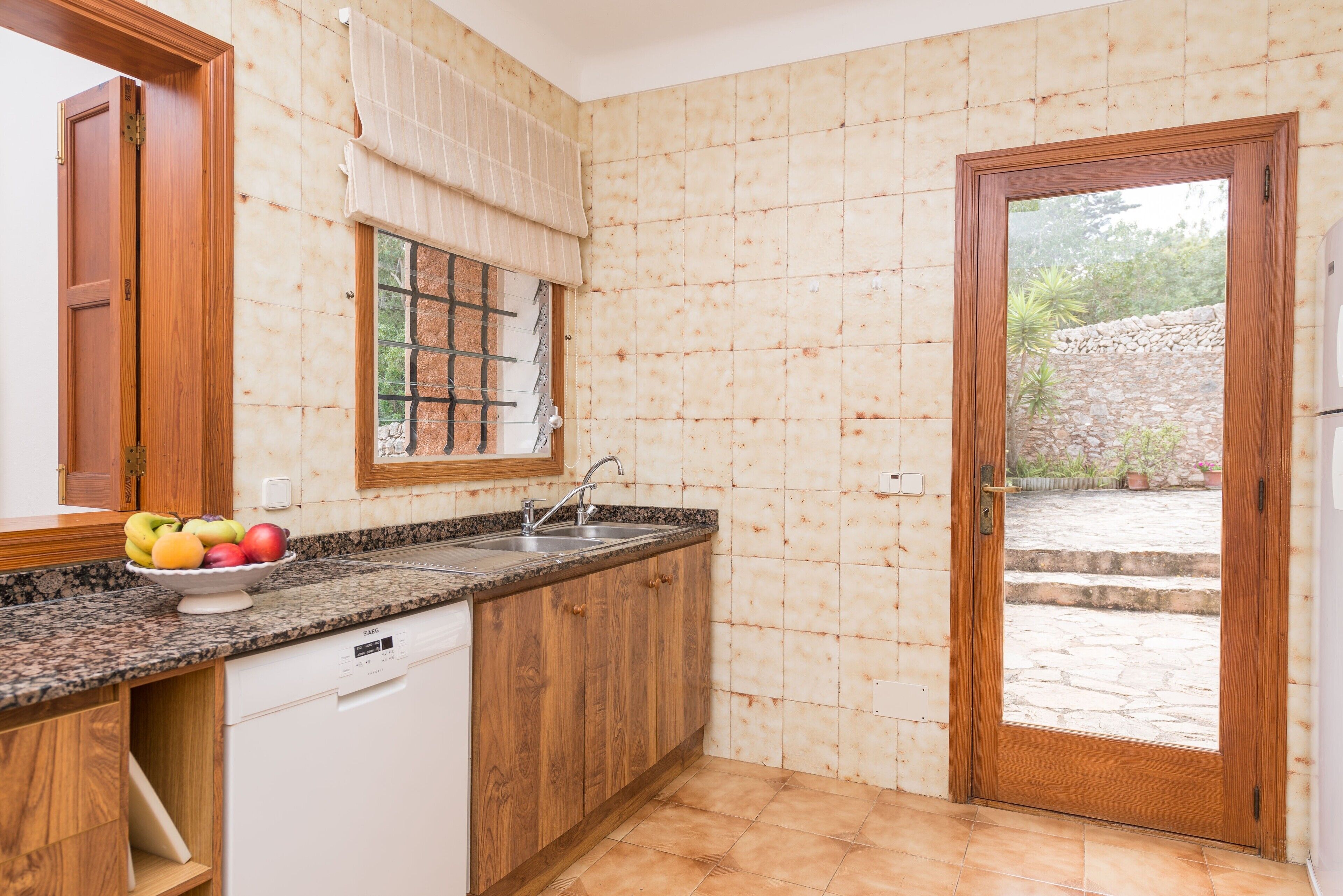 Eine Küche mit Holzschränken, einer Granit Arbeitsplatte, einem eingebauten Geschirrspüler und einem Fenster mit Blick auf eine Steinsäule und Vegetation draußen.