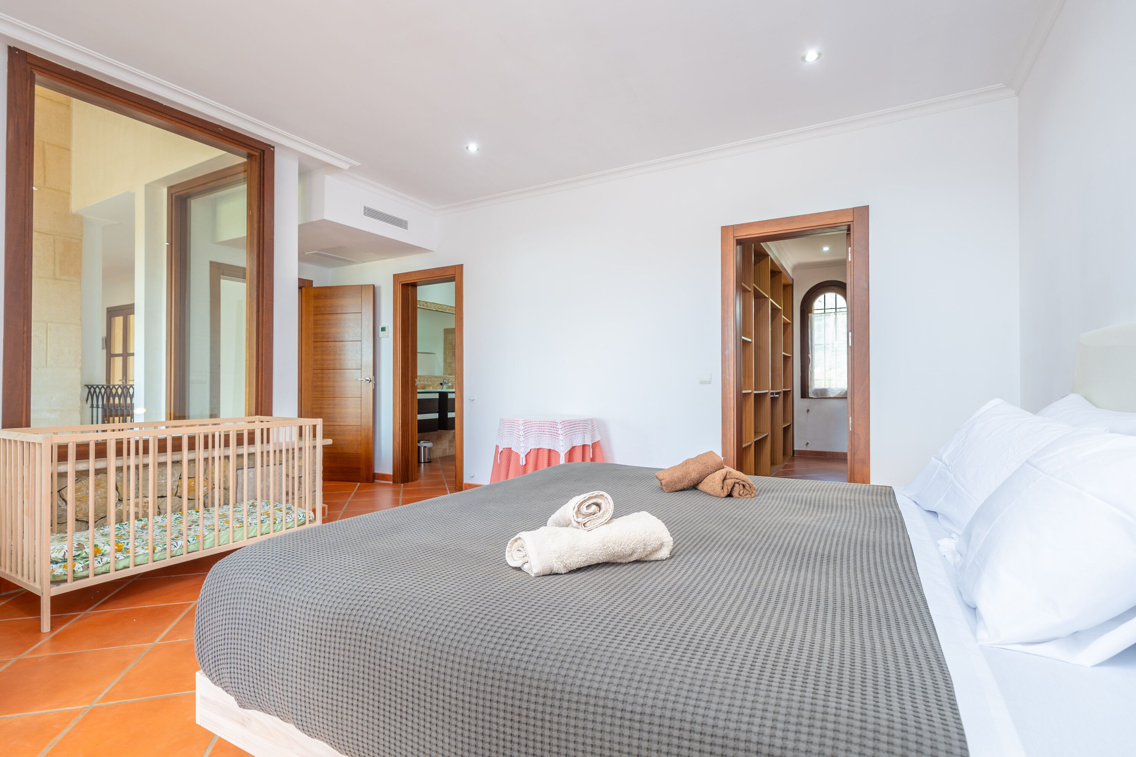 A hotel room with a large bed, a wooden crib, and a bathroom visible through an open door.