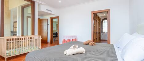 A hotel room with a large bed, a wooden crib, and a bathroom visible through an open door.