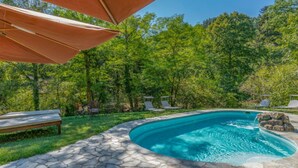 A swimming pool with stone tiles, surrounded by grass and trees.
