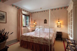 A four-poster bed with a floral bedspread, a small bedside table with a lamp, and a wall-mounted light fixture.