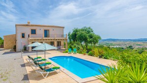 A villa with a swimming pool, outdoor seating, and a view of the countryside.
