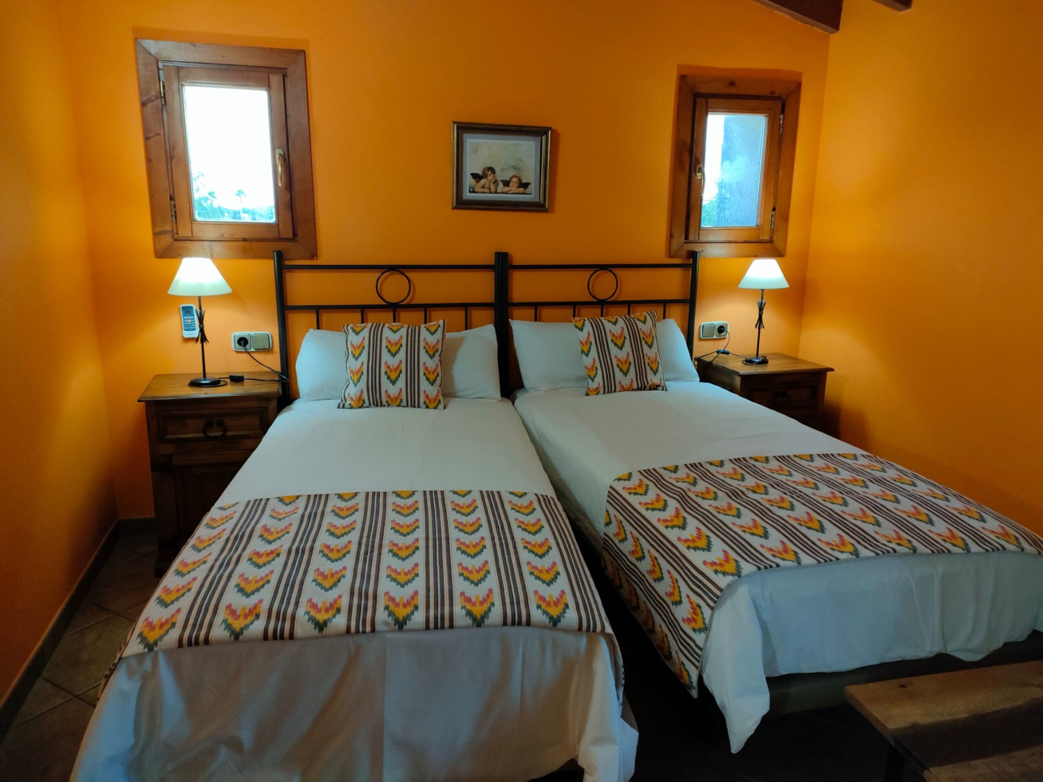 Ein Hotelzimmer mit zwei Betten, jeweils mit gemusterten Tagesdecken, zwei Nachttischlampen und einem gerahmten Bild an der Wand.