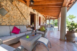 A covered outdoor seating area with stone walls, wicker furniture, and a potted plant.