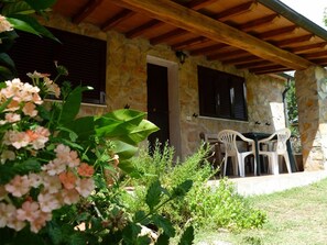 A stone building with a wooden roof, a door, and two windows with shutters. There is a table and two chairs outside. - Beautiful private villa for 7 people with private pool, WIFI, pets allowed and panoramic view (Pitigliano)