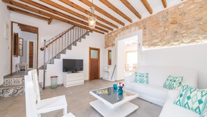 A spacious living room with a white sofa, a glass coffee table, and a TV. A staircase with wooden beams leads to another room. - CAN DIANA - Vacation home with private pool in peaceful town. Free WiFi (Campanet)