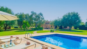 Ein Poolbereich mit Liegestühlen, einem klaren blauen Pool und einem gepflegten Garten mit Bäumen und einem Gebäude im Hintergrund.