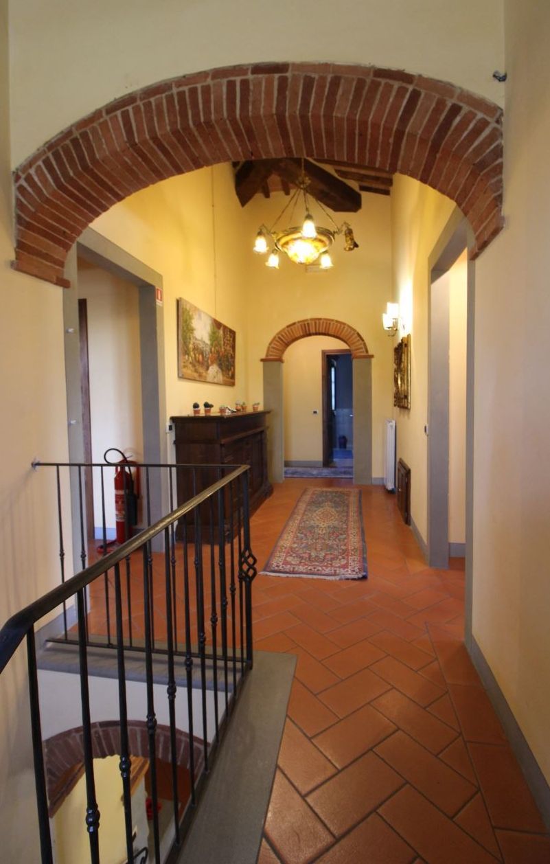 A hallway with a brick archway, a staircase with a railing, a fireplace, and a hallway rug.
