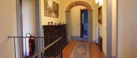 A hallway with a brick archway, a staircase with a railing, a fireplace, and a hallway rug.