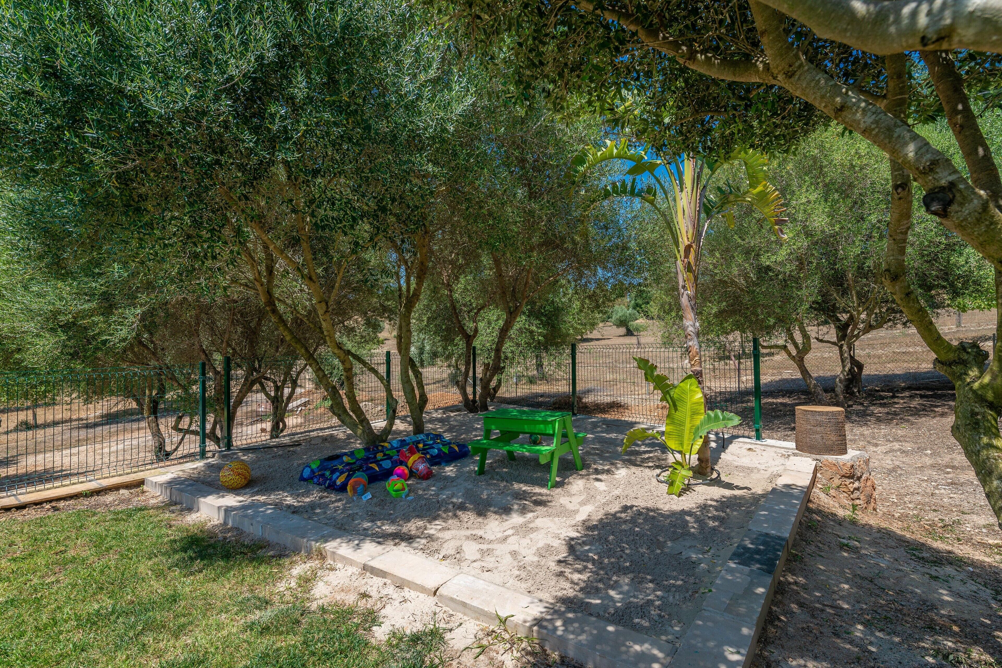 A playground with a green bench, a ball pit, and a fenced area with trees.
