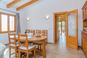 A dining area with a wooden table and chairs, a kitchen area with wooden cabinets, and a view of the outdoors through a door.