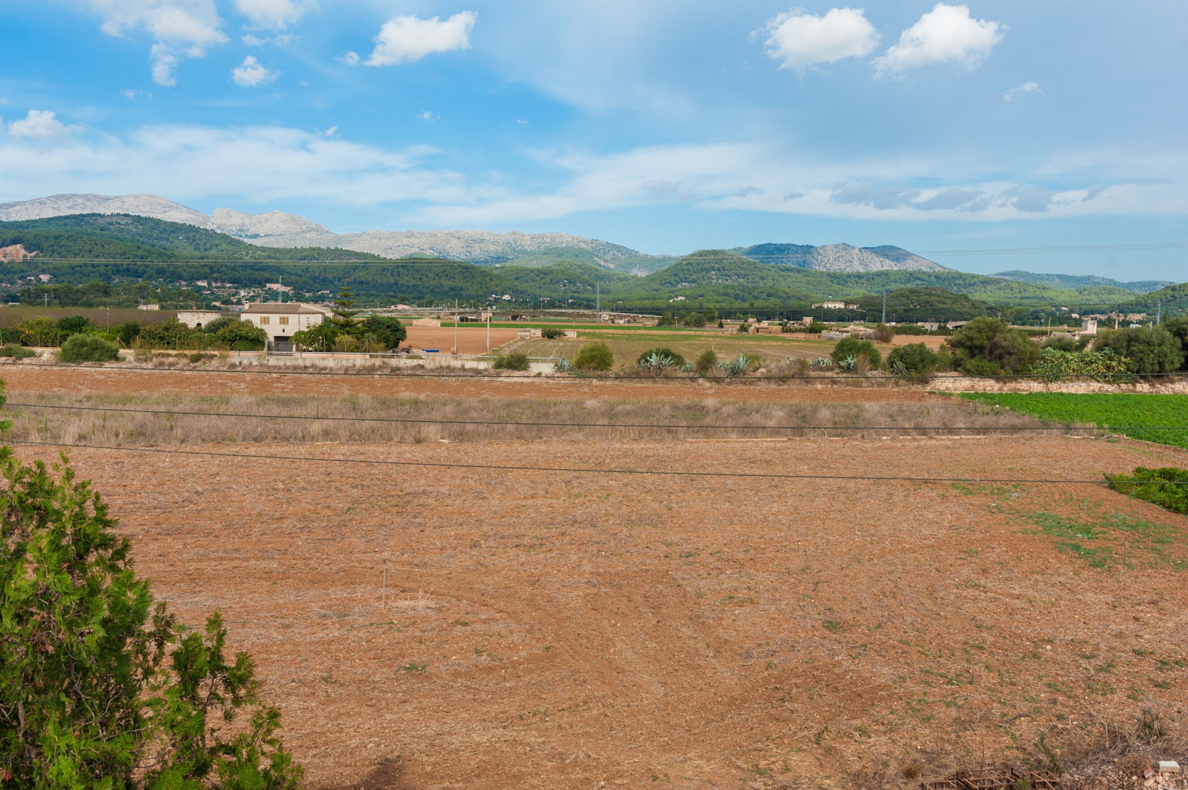 A rural landscape with fields, a few buildings, and mountains in the background.