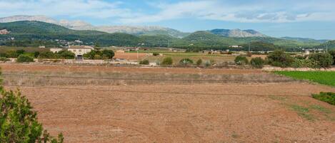 A rural landscape with fields, a few buildings, and mountains in the background.