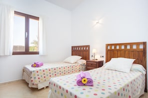 A hotel room with two beds, each with a polka dot bedspread and a flower on the bed. There is a window with curtains, a nightstand with a lamp, and a wooden headboard.
