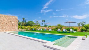 A swimming pool with lounge chairs and umbrellas, surrounded by greenery and a stone wall. - CAN GUSTI - Villa with private pool in Manacor. Free WiFi. (Manacor)