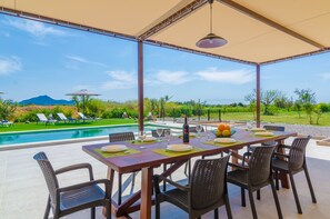 Un área de comedor al aire libre con vista a la piscina, mesas dispuestas con platos y vasos, y sillas.