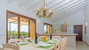 A dining area with a long table set for six, a chandelier, and a view through large sliding glass doors. - CAN GUSTI - Villa with private pool in Manacor. Free WiFi. (Manacor)
