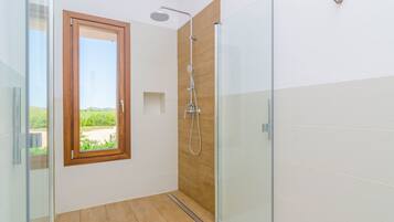 A modern bathroom with a glass shower enclosure, wooden paneling, and a window offering a view of greenery.