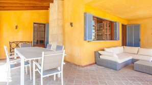 An outdoor patio area with a dining table and chairs, a wicker sofa, and a window with shutters. - FINCA CAN POL - Villa with private pool in Inca. Free WiFi (inca)
