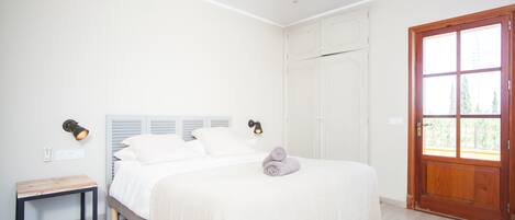 A bedroom with a bed, bedside table, and a door leading to a balcony.