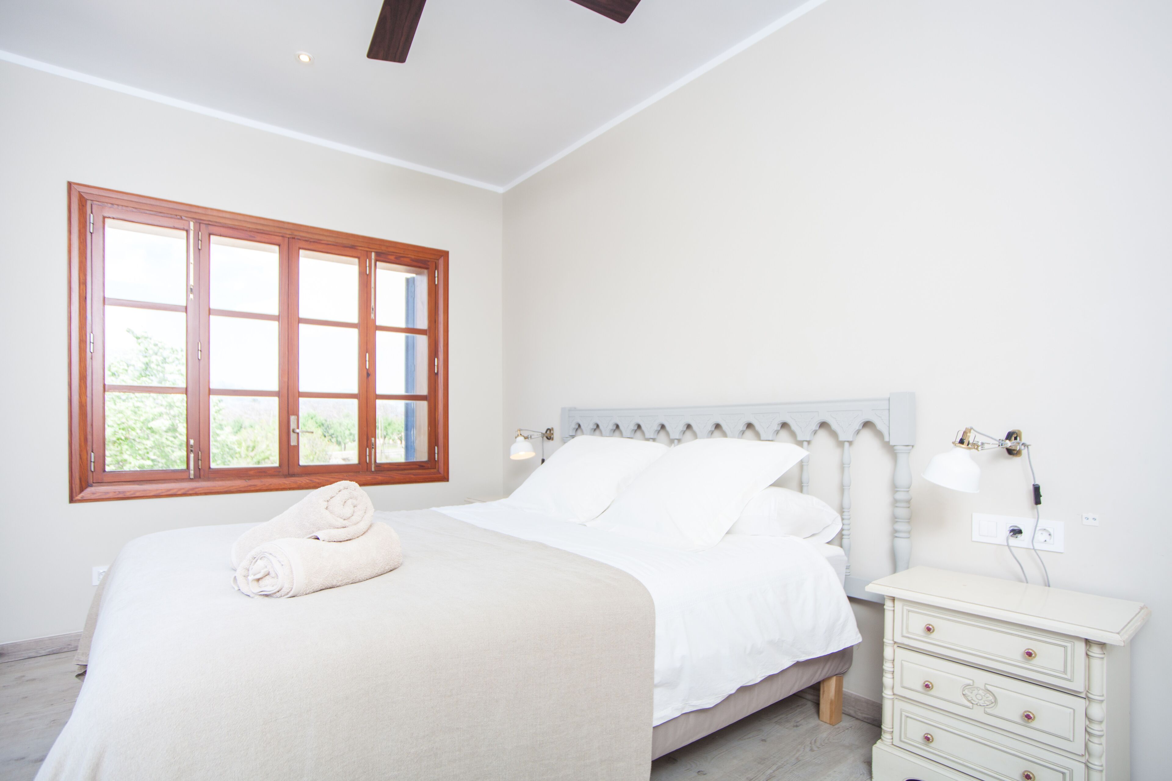 Un dormitorio con cama, mesita de noche, lámpara y ventana con vistas a la vegetación.