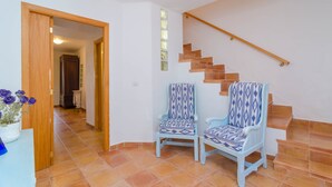 A staircase with wooden steps and a handrail, leading to an upper floor. Two chairs with patterned upholstery are placed near the staircase.