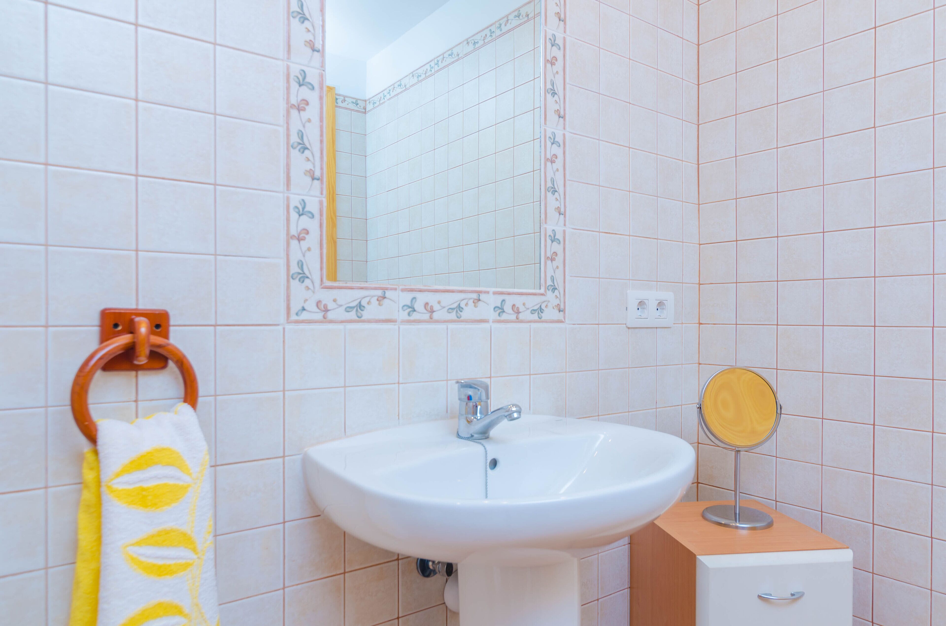 Un baño con un lavamanos blanco, un espejo y un perchero con una toalla amarilla.