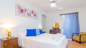 A neatly arranged bedroom with a bed, bedside tables, a ceiling fan, and a window with curtains.