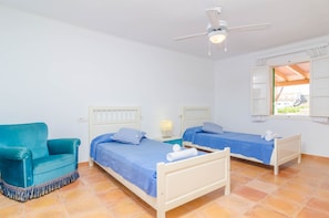 A room with two beds, a sofa, a ceiling fan, and a window with shutters.