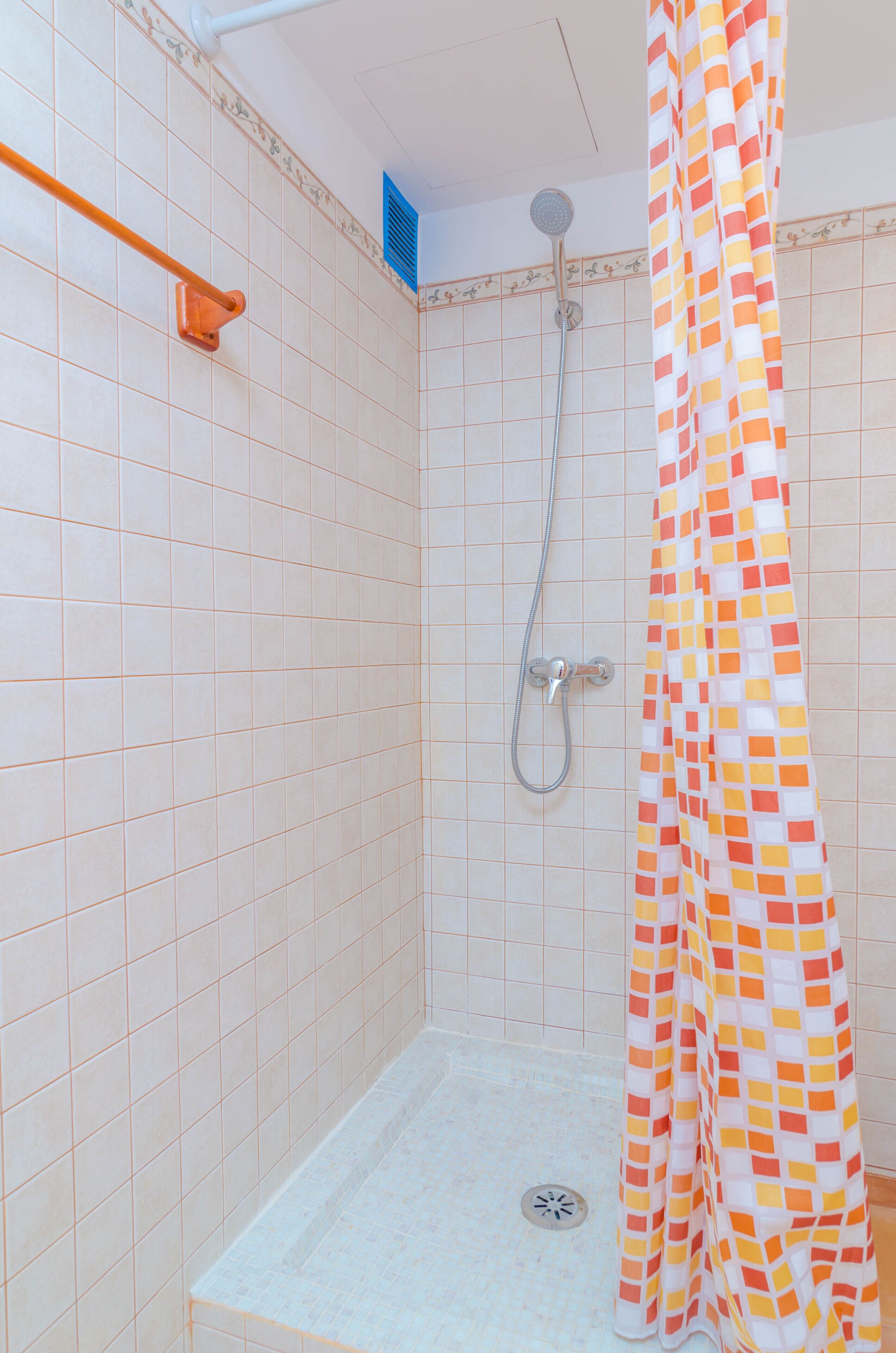 Eine Dusche mit gefliesten Wänden, einer Duschbrause, einer Handbrause und einem bunten Duschvorhang.