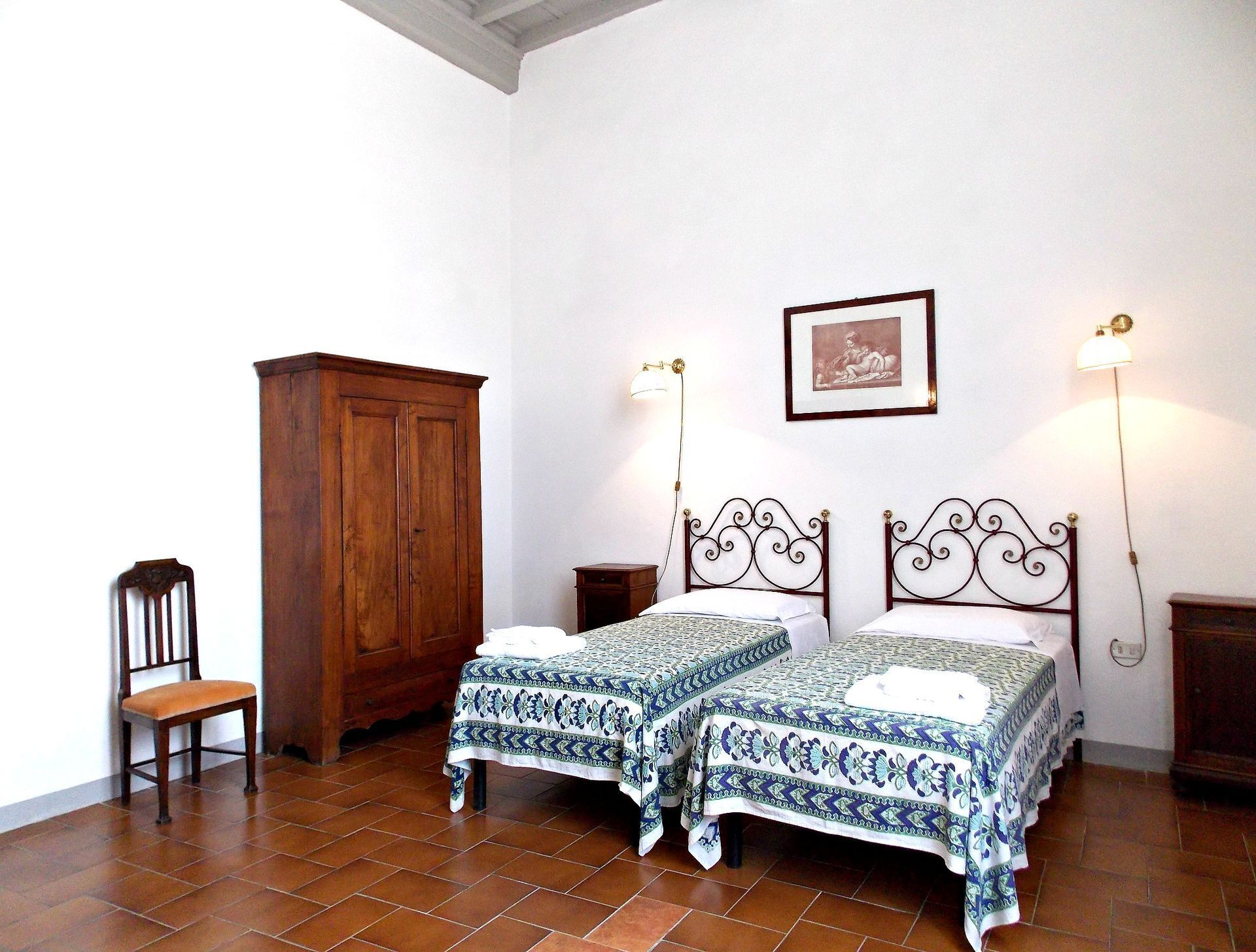 A bedroom with two beds, a wooden wardrobe, a chair, and a framed picture on the wall.