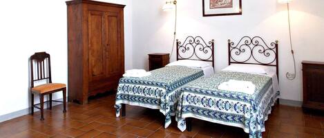 A bedroom with two beds, a wooden wardrobe, a chair, and a framed picture on the wall.