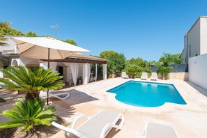 En swimmingpool med liggestole, en pergola med et markise og en palme.