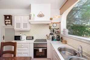 Una cocina con armarios blancos, horno empotrado, un lavamanos y una ventana con vistas a árboles.