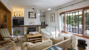 A cozy living room with a TV, sofa, and coffee table. There is a fireplace, a bookshelf, and a window with a view of the outdoors. - VILLA GARBA - Villa with private pool in Felanitx. Free WIFI (Felanitx)