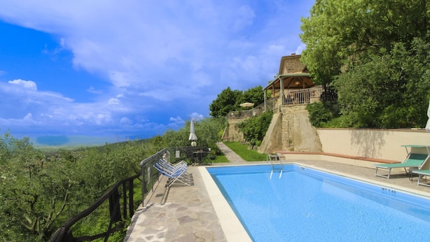 A swimming pool with a stone deck, a stone wall, and a view of the landscape.