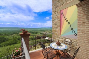 A balcony with a view of a green landscape, a table with chairs, and a colorful sign on the wall.