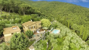 A two-story house with a swimming pool, surrounded by lush greenery and hills.