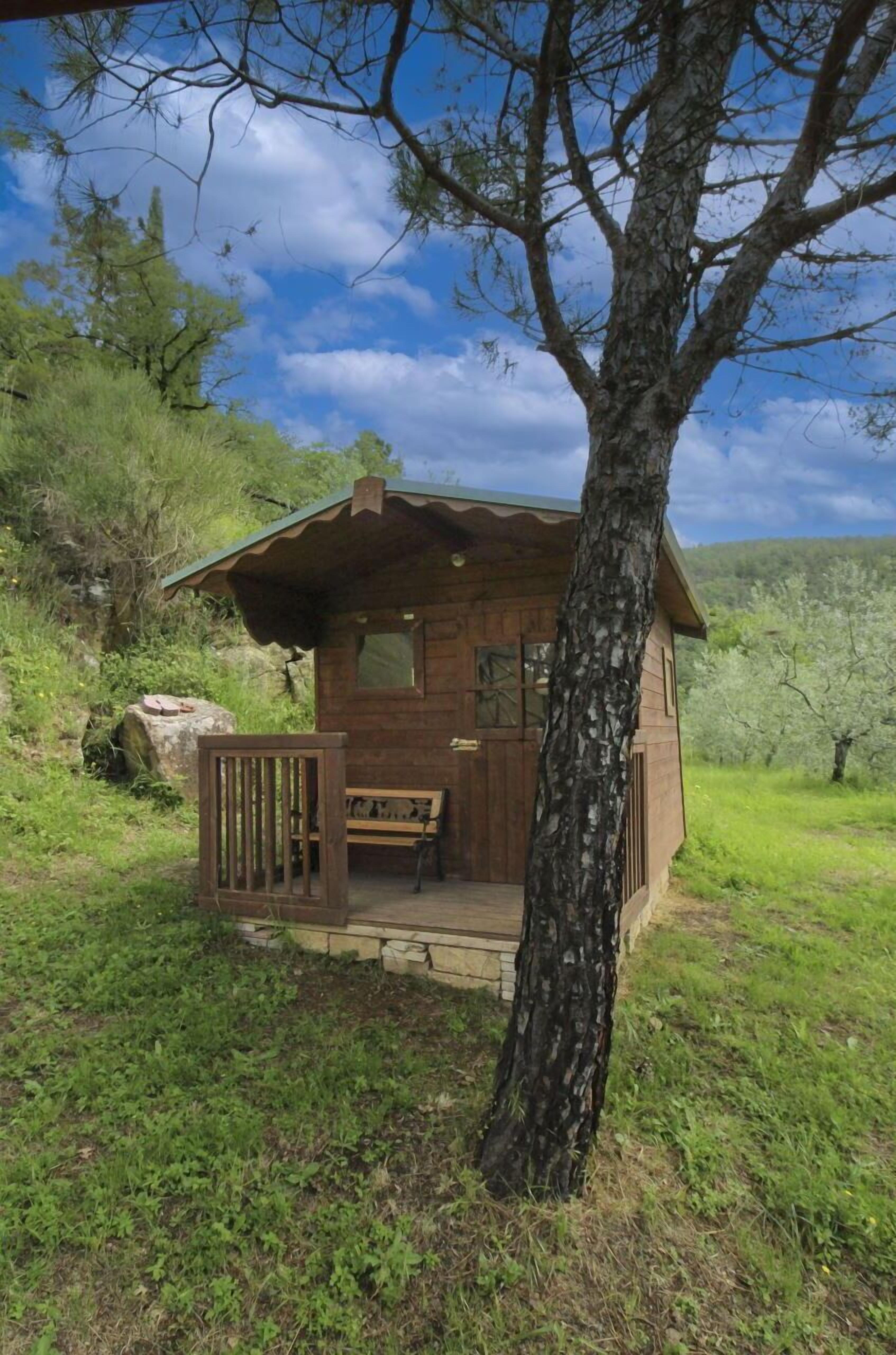 A wooden cabin with a porch, a bench, and a view of the surrounding greenery and hills.
