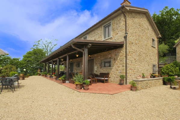 A stone building with a covered patio, outdoor seating, and potted plants.