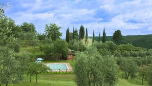 Une villa avec piscine, entourée d’oliviers, et une maison en pierre en arrière-plan.