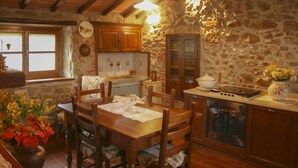 Une cuisine rustique avec des murs en pierre, des armoires en bois, une table à manger avec des chaises et un four encastré.