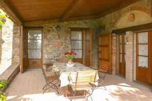 A stone-walled patio with a wooden table, chairs, and a bench.