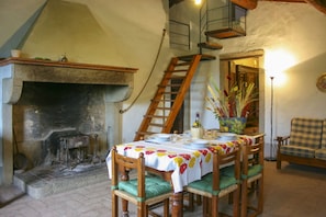 Un coin repas agrémenté d’une cheminée, d’une table en bois dressée pour quatre personnes et d’une chaise dotée d’un coussin à carreaux.
