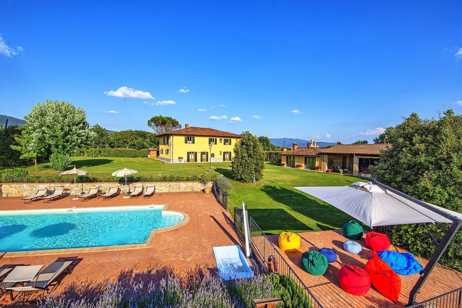 A pool area with lounge chairs, a small pool, and a large house with a garden.