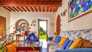 Una sala de estar acogedora con techo de madera, un sofá floral, una mesa de madera y vista a un jardín por una puerta abierta.